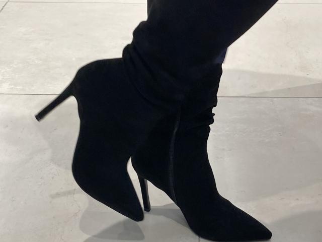 Gros plan des jambes de DeesseBleue et de ses bottes noires à talons hauts et pointus, avec des talons aiguilles, debout sur sol blanc et brillant.
ombres sous les bottes, soulignant leur forme et leur texture..