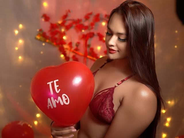 Yessica Belltran, con lunghi capelli neri, indossa un reggiseno rosso in pizzo e tiene un palloncino rosso a forma di cuore con la scritta "TI AMO". scritto sopra.
sfondo: luci fatate calde, foglie rosse sfocate. Incredibilmente sexy..