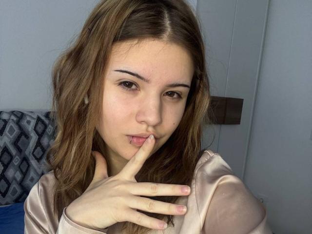 BarrieGromley with medium brown wavy hair, light skin, and brown eyes, biting finger with a seductive look, wearing a shiny beige top, right hand near face, subtle sexual tension.