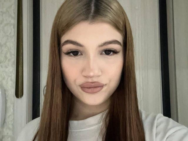 Close-up of JaclynCerasuolo, a young woman with long brown hair, full lips, and thick eyebrows. She's wearing a white turtleneck, looking directly at the camera with a subtle smile.