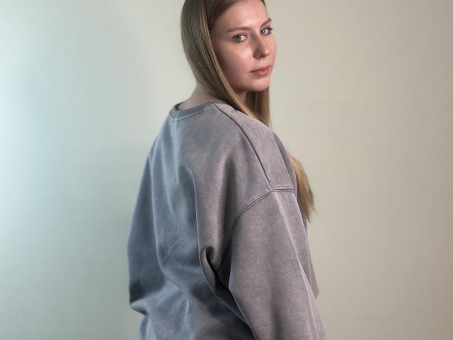 Photographie de Calista Torn avec de longs cheveux bruns, portant un sweat gris ample, regardant par-dessus son épaule. Expression subtile et sensuelle, éclairage doux, et une légère ombre sur la droite..