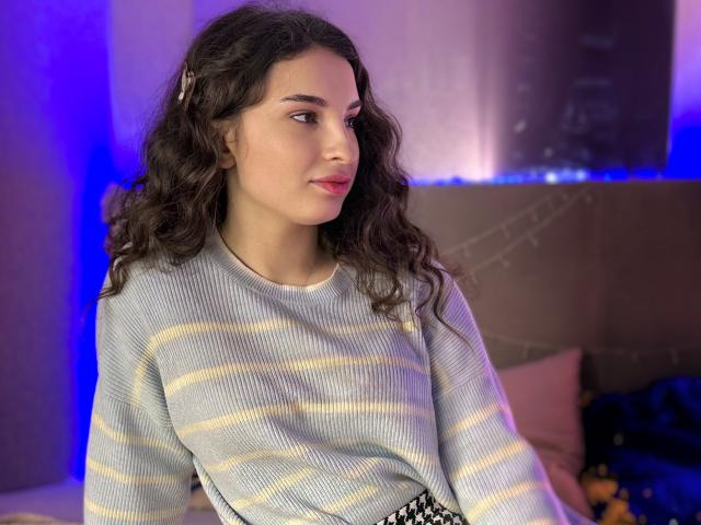 Fotografia di Josephine Rowe, una giovane donna con lunghi capelli neri ondulati, che indossa un maglione a righe bianche e gialle. Ha un profilo laterale, rivolta verso sinistra, con una sottile luce blu sullo sfondo. La sua espressione è neutra, con un accenno di fascino..