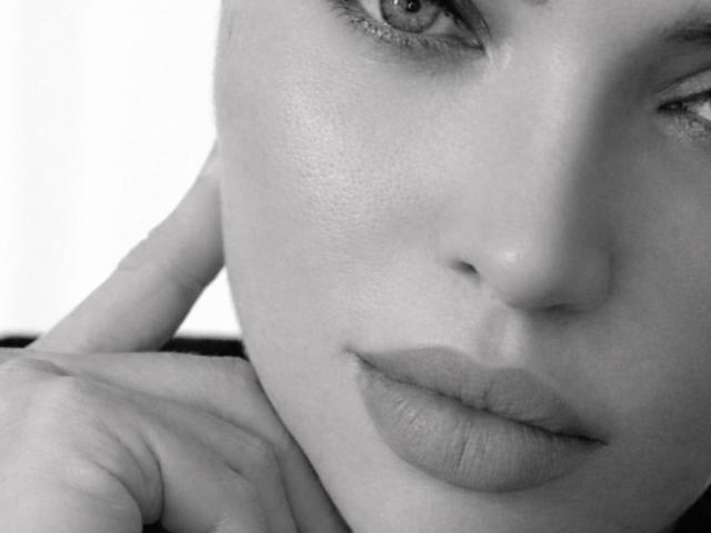 Primo piano del viso di Axinia, con una tonalità blu, che si concentra sulle sue labbra leggermente dischiuse e sulla mano appoggiata sulla guancia. I suoi occhi sono socchiusi, e trasmettono uno sguardo sensuale e provocante..