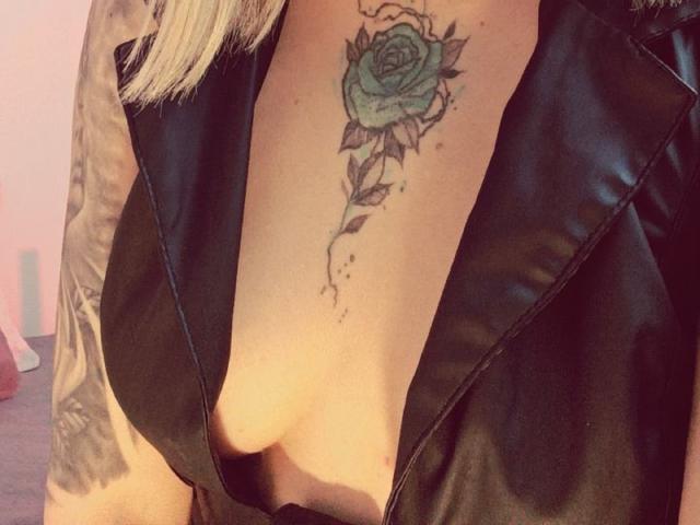 Close-up of KayleeM's arm with a detailed green and black rose tattoo on the inner bicep. KayleeM's wearing a black leather vest, exposing fair skin and blonde hair. Fucking sexy tattoo.