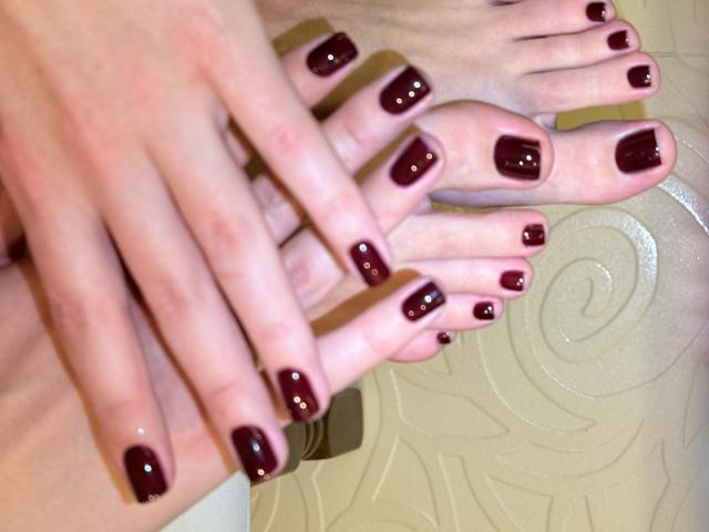 Close-up of MargoFun's feet with shiny black nail polish, crossed over each other. MargoFun's hands rest on top, fingers splayed. Glossy, wet texture on the feet and hands.