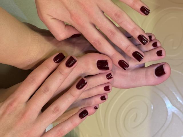 Close-up of MargoFun's hands and feet with glossy dark red nail polish. Fingers rest gently on toes, creating a sensual tension. Pale skin, smooth texture, and soft lighting.