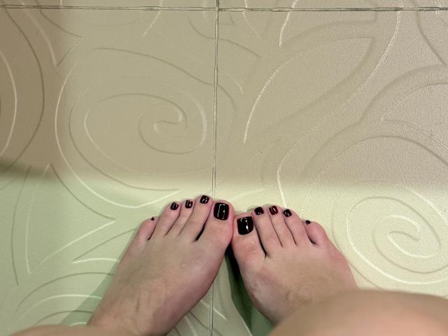 Close-up of MargoFun's feet on a glossy, swirling-patterned floor. MargoFun has black-painted toenails, with slightly dirty feet. Feet are pressed together, creating a suggestive, intimate vibe.