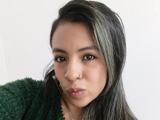 Close-up of MeganFerrerr, Asian woman with long black hair, nose ring, and dark eyes, wearing a green fuzzy sweater, lips slightly pursed, white background, high contrast, sexy and intense gaze.