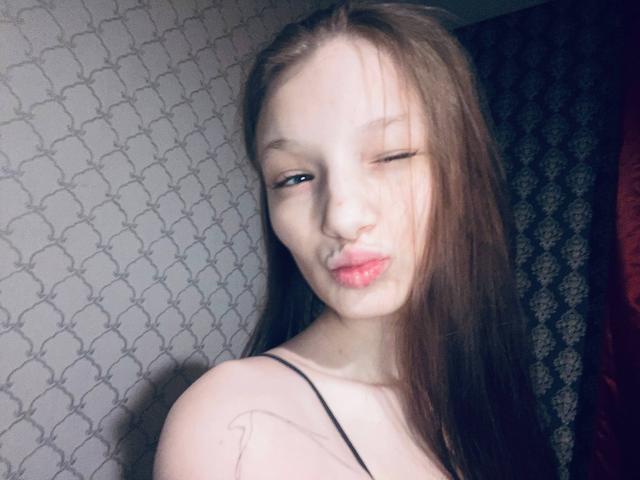 MelbaCaffee ha la pelle chiara, i capelli lunghi castani e un'espressione maliziosa con le labbra leggermente socchiuse e di colore rosa. Indossa una maglietta con spalline sottili, che proietta ombre drammatiche sul suo viso. La tensione sessuale è evidente..