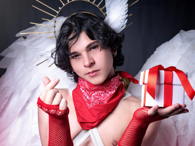 Luke Howlandy, un cosplayer de piel clara con cabello negro corto, lleva un halo dorado, guantes de malla roja y una bufanda roja. Sosteniendo un regalo blanco con un lazo rojo. Una vibra angelical, increíble..
