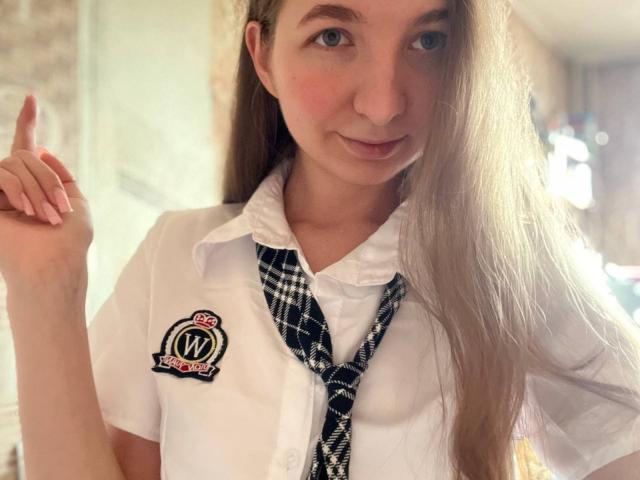 Fotografie von Maryanne, einer attraktiven, jungen Frau mit langen, braunen Haaren, die ein weißes Schulhemd mit schwarzem Krawattenknopf trägt. direkt in die Kamera blickend, Mittelfinger erhoben, sexy, provokativer Ausdruck.