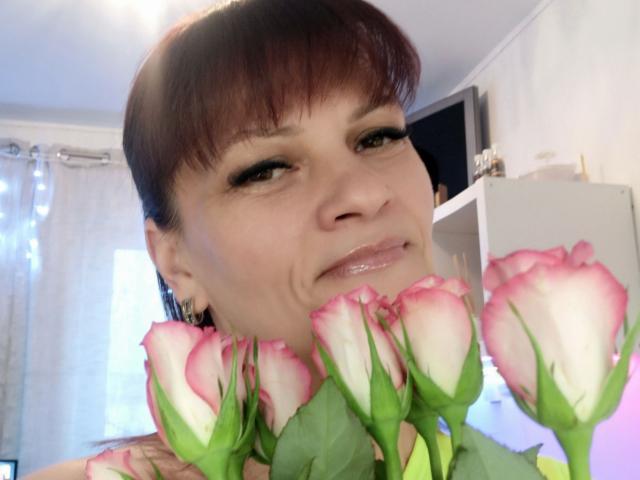 Close-up van LaraaFox, aantrekkelijk, die roze en witte tulpen voor haar gezicht vasthoudt, met een lichte glimlach en glanzende lipgloss. Heldere binnenverlichting, witte gordijnen op de achtergrond.