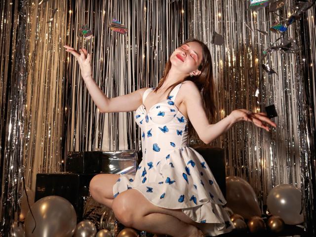 AmbeerWood kneels on the floor, wearing a white dress with blue star patterns, reaching up with one hand, eyes closed, lips parted. Sparkly background, balloons, and strings. Fucking sexy.