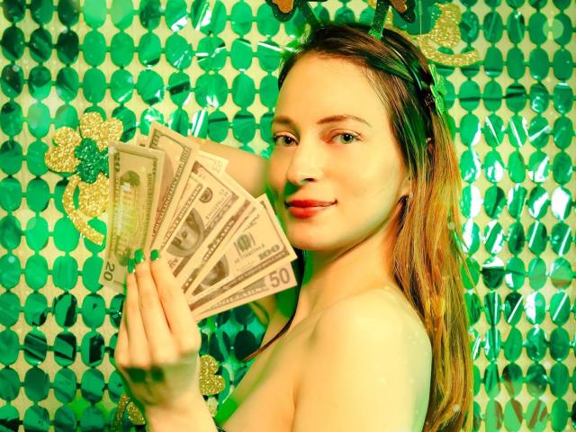 AmbeerWood, topless with long brown hair, holds a fan of cash in front of a green and gold patterned background. She's looking at the camera with a seductive smile. Bright colors.