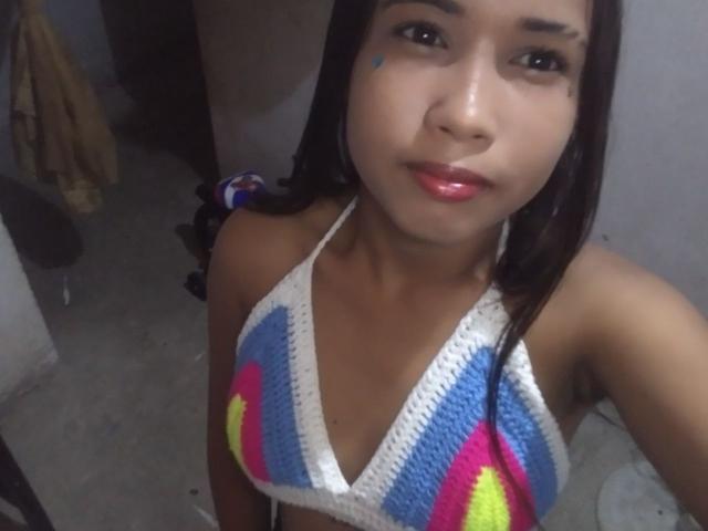 Close-up photo of SofiaPerezLov with brown skin, black hair, and blue face paint. She wears a colorful crochet halter top, looking up with red lips. Sexual tension, cock hinted by top.