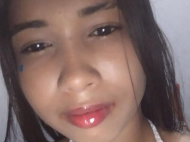 Primo piano del viso di SofiaPerezLov, con capelli castano scuro, labbra rosse lucide e un piccolo segno blu sulla guancia. Ha un'espressione sensuale, con le labbra leggermente dischiuse, che trasmette una forte tensione sessuale..