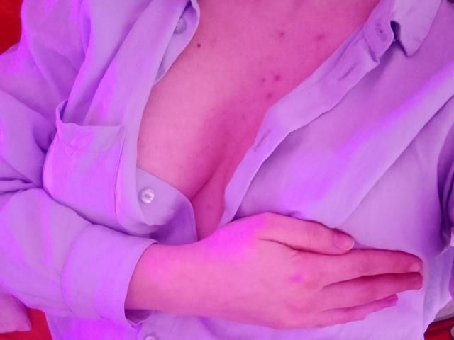 Close-up of Marriam's chest, wearing an unbuttoned white shirt, revealing ample cleavage and pinkish skin with slight blemishes. One hand rests on the shirt, creating a suggestive, intimate pose.