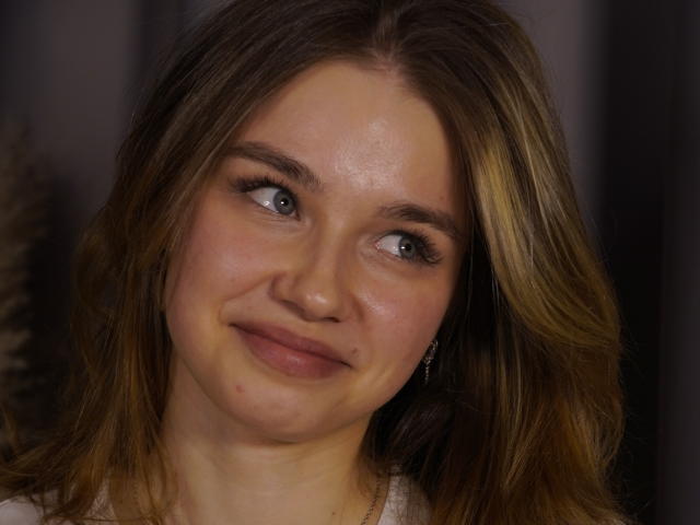 Close-up foto van JennyOsmun, een jonge vrouw met lichtbruin haar, blauwe ogen en een lichte glimlach. Ze heeft een paar kleine puistjes op haar wangen. Haar huid is licht glanzend..