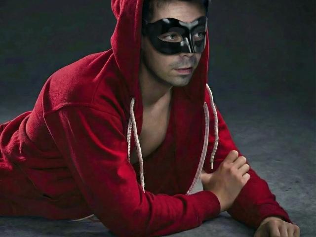 Dannyboy20-fun-hot è sdraiato su una superficie scura, indossando una felpa rossa e una maschera nera, con occhi intensi e un'espressione seria. espressione.
la sua mano destra è appoggiata a terra, piegata e pronta all'azione..