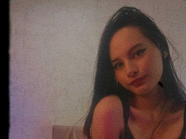 Foto van LunaBellee, close-up, licht gekanteld hoofd, lang zwart haar, verleidelijke uitdrukking, rode lippen, onbedekte schouders, zachte roze en paarse verlichting, korrelige textuur, subtiele seksuele spanning, intieme sfeer.
