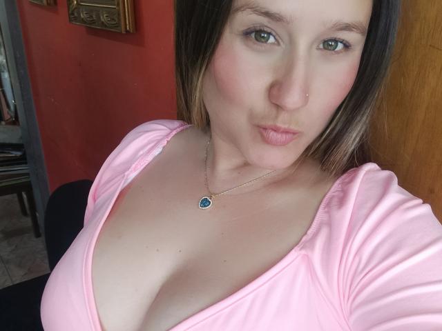 Close-up selfie of AlexaHotSeins, with fair skin and blue eyes, wearing a low-cut pink top revealing ample cleavage. She has a nose ring and a blue pendant necklace. Fucking sexy look.