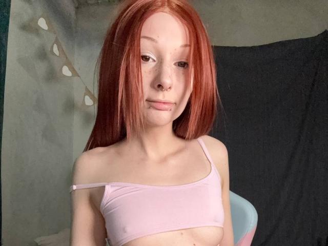 Foto van een jonge vrouw met glad, rood haar, die een witte top draagt met een open schouder, een lichte huid heeft en een zelfverzekerde uitstraling. uitdrukking.
ze heeft kleine borsten en een subtiele glimlach. Verdomd aantrekkelijk..