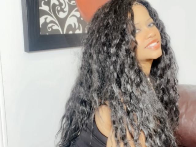 Cincia69, una donna attraente con lunghi capelli neri ricci, che sorride con le labbra rosse, indossa una maglietta nera ed è appoggiata a divano in pelle rossa.
opere d'arte decorative in bianco e nero sullo sfondo..