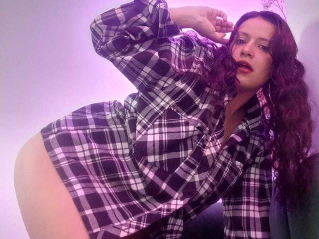 AriannaSeete with long, wavy brown hair, wearing an unbuttoned black and white plaid shirt, leaning forward, hand in hair, exposing bare hip, seductive pose, intense gaze, purple lighting.