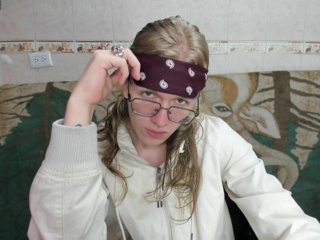 JinnLook, vestindo um moletom branco, ajusta um lenço roxo escuro com padrões brancos sobre o cabelo castanho desgrenhado, segurando óculos sendo segurados com uma mão, aparência molhada, sexy, parede com azulejos e arte abstrata ao fundo..