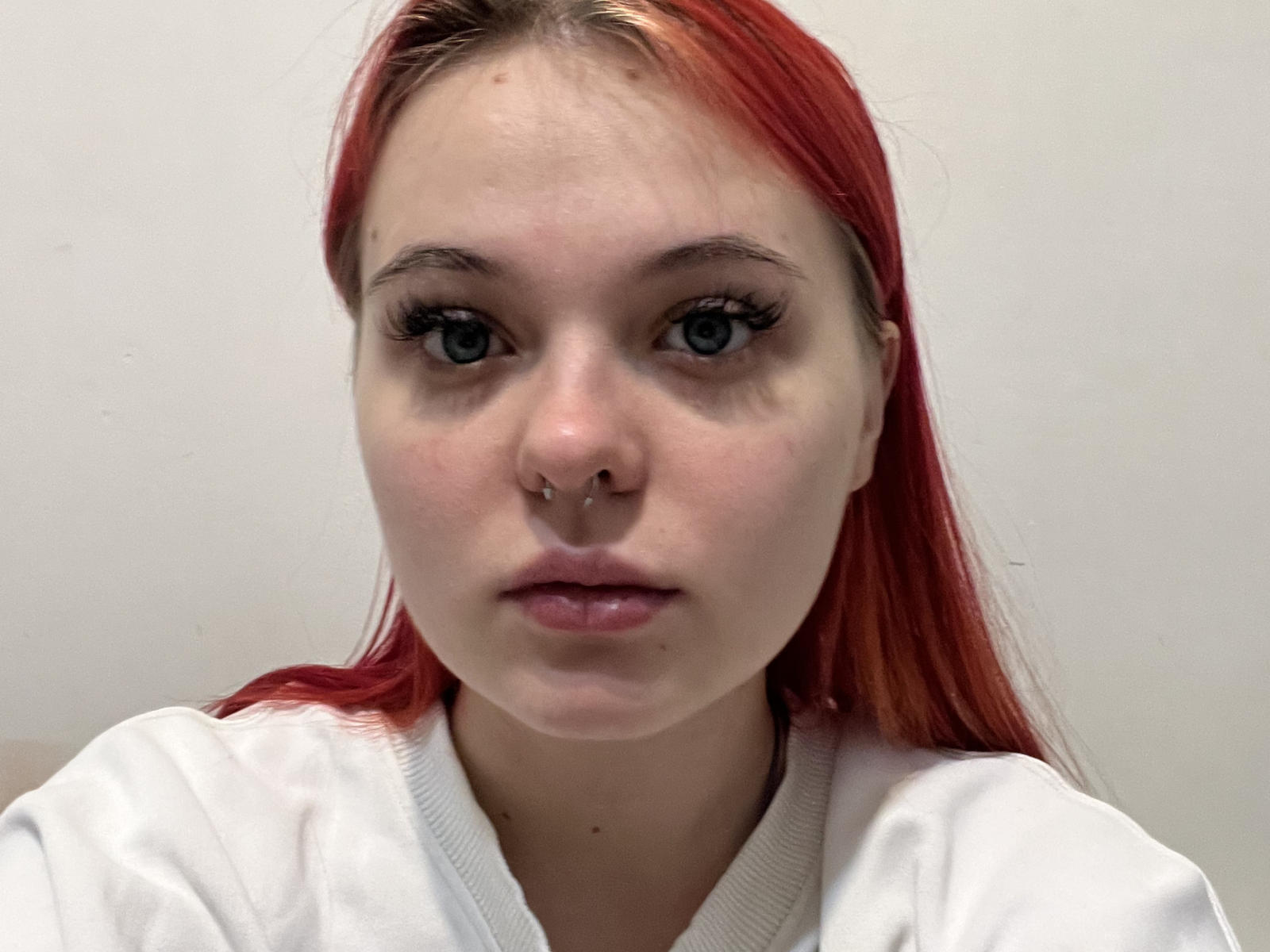 Primer plano de Diane Tardif, con cabello rojo, vistiendo una camisa blanca, mirando directamente a la cámara con una expresión neutra. Su nariz tiene perforaciones. La imagen tiene un alto contraste y una textura ligeramente granulada..