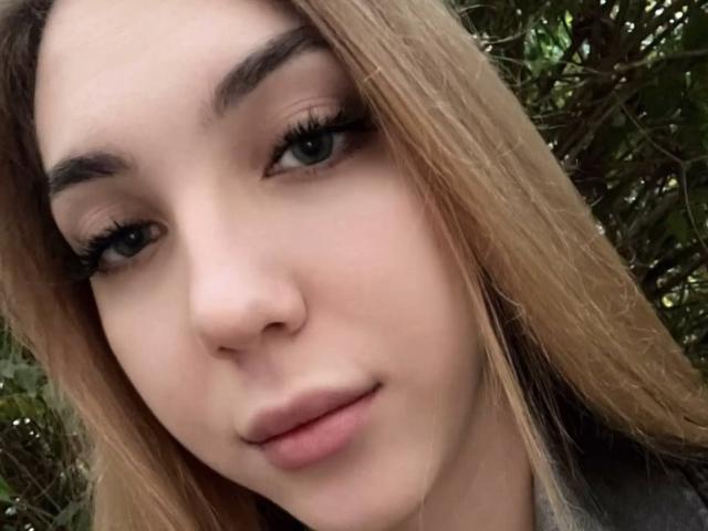 Primo piano di Alease Benson con la pelle chiara, labbra piene e lunghi capelli castani. Lei guarda direttamente la fotocamera con gli occhi socchiusi, un leggero sorriso e sopracciglia scure e arcuate. Messa a fuoco in primo piano.