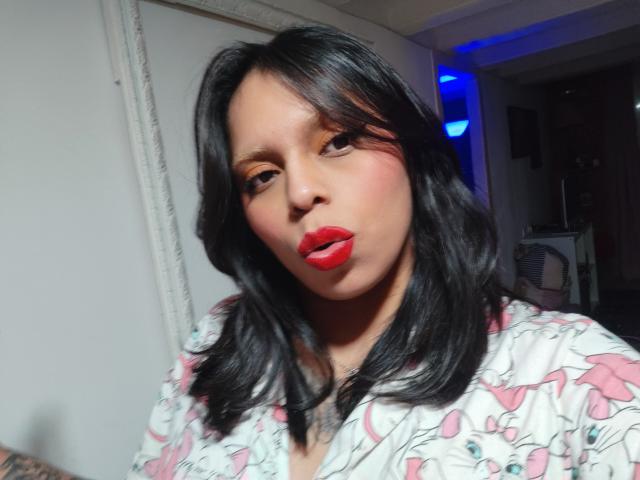 Close-up of Chili, a curvy woman with medium brown skin and black hair, wearing a white floral shirt, red lipstick, and a slight pout, casting a sexy, seductive gaze.
