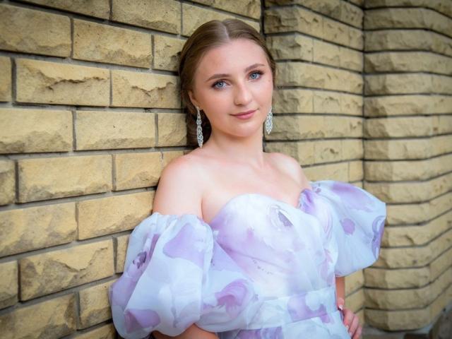 SamuelaBella with fair skin, blue eyes, and brown hair, leaning against a brick wall. Wearing an off-shoulder white dress with puffy sleeves, wearing dangling earrings. Seductive, soft smile.