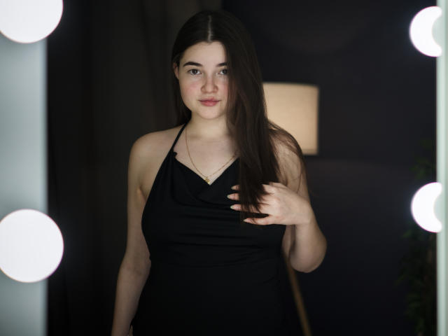 Fotografia de LizabethAmore com cabelos longos e escuros, vestindo um vestido preto de alça, em frente a luzes brilhantes, com a mão tocando em seu peito, fundo escuro, tensão sexual, expressão sedutora..