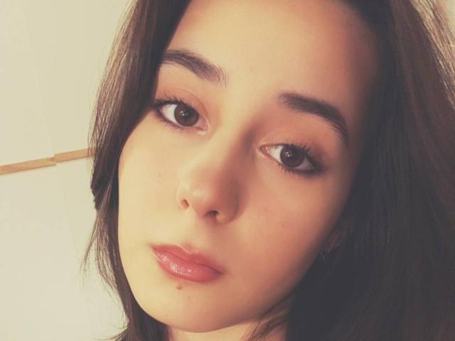 Close-up of TrinidadGuerini's face with light skin, dark brown eyes, and full pink lips. She has long dark hair and a neutral expression. The lighting highlights her smooth skin. Fucking sexy.