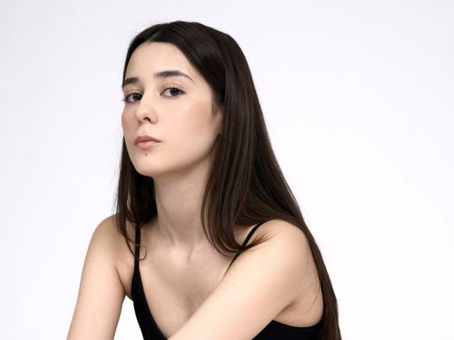 TrinidadGuerini ha lunghi capelli neri e lisci, pelle chiara e un'espressione seria. Indossa una canotta nera, con le spalle scoperte. È rivolta leggermente verso sinistra. Sfondo bianco.