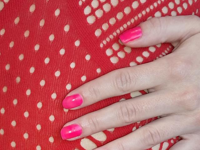A close-up of Amberia's hand with bright pink nail polish resting on a red fabric with white polka dots. The hand's fingers are spread, highlighting the glossy nails and textured fabric.