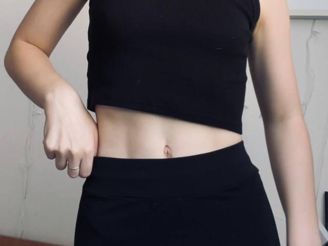 Photo en gros plan de la partie médiane du corps de DeeannMilloy, vêtue d'un haut court noir et d'un pantalon noir. Sa main gauche repose sur sa hanche, révélant son ventre plat et son nombril. La peau est claire et tonifiée.
.