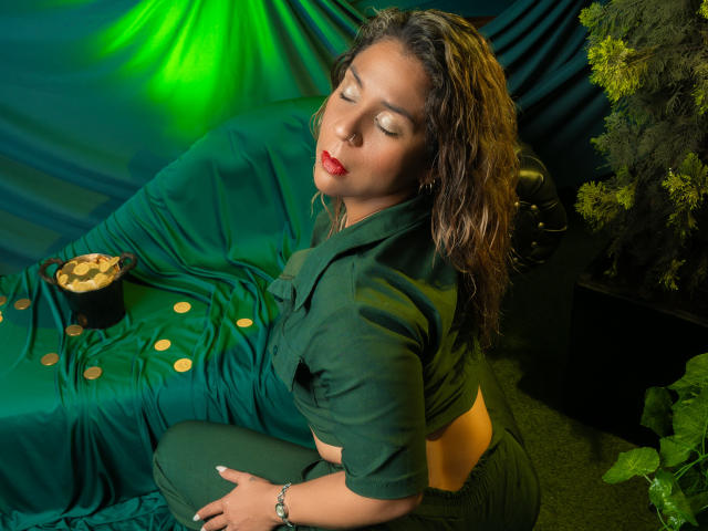 Muitas mulheres, com cabelo preto molhado, batom vermelho e roupa preta, sentadas em uma superfície coberta de verde. A luz verde e amarela realça seus olhos fechados e sua expressão relaxada. A mão dela repousa sobre a coxa..