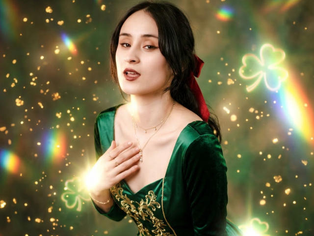 Annie Lamberth, met een lichte huid en zwart haar, draagt een groene fluwelen jurk met gouden borduursel, met haar hand op haar borst, stralend. lichteffecten op de achtergrond, aantrekkelijk, levendig, kleurrijk, zelfverzekerde pose.