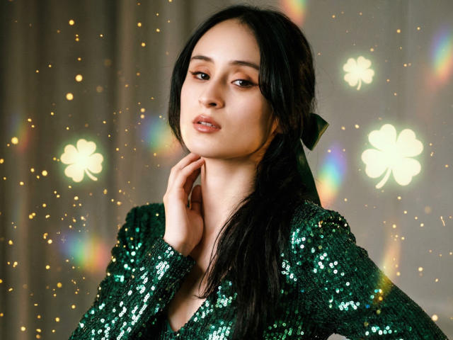 Annie Lamberth, een prachtige Aziatische vrouw met lang zwart haar, kijkt verleidelijk in de camera. Ze draagt een glanzend zwart top met pailletten, met felle lichten en glitters op de achtergrond. Heel erg aantrekkelijk..