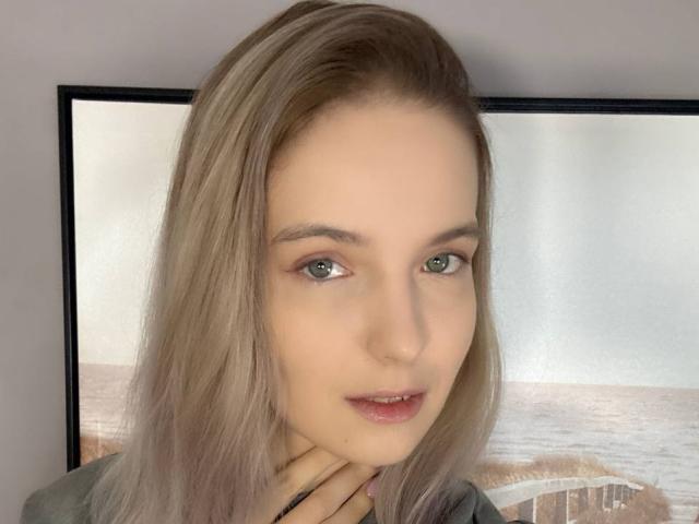 Foto van Nicole Spritzer, close-up, lichtbruin haar, blauwe ogen, lichte huid, lichte glimlach, hand op de nek, zacht. make-up, heldere achtergrond met een raam, nonchalante pose, lichte seksuele spanning, aantrekkelijk.