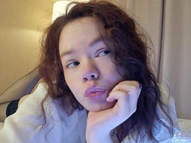 Close-up of CoreyRounsaville with messy brown hair, pouty lips, and hand resting on chin. Blue lighting on face, wearing white shirt. Seductive gaze, slightly disheveled look, intense expression.