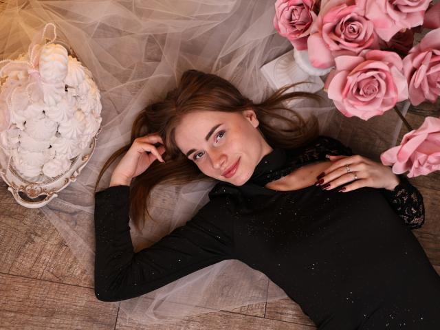 MargaritaKis ligt op haar rug, met bruin haar, en draagt een zwarte jurk, omringd door roze rozen en een witte, gloeiende lantaarn. Ze heeft een verleidelijke glimlach, rode nagels en een ring..