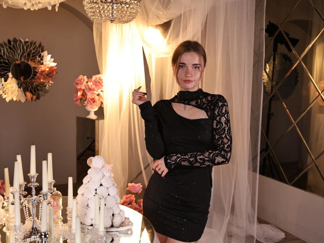 MargaritaKis se tient dans une pièce faiblement éclairée, vêtue d'une robe noire en dentelle avec une découpe, et tient un couteau. Des bougies, des roses et un lustre sont en arrière-plan. La tension sexuelle est palpable..