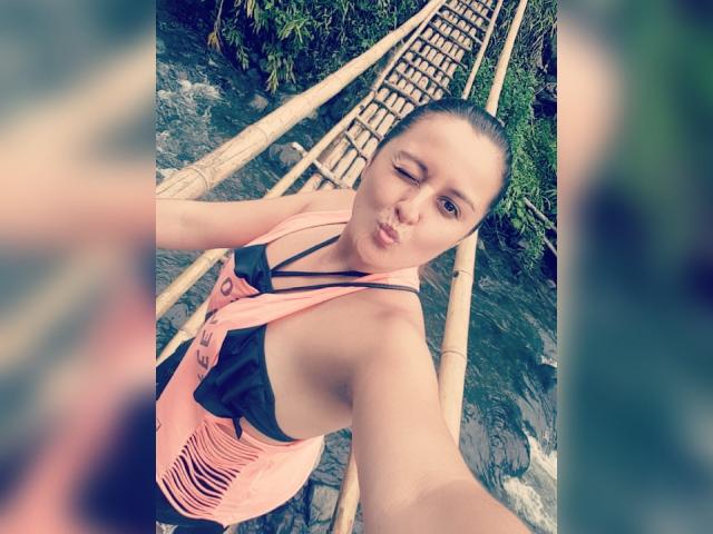 LaurenSpitz takes a selfie from above, wearing a pink and black swimsuit, holding a paddle. Her wet hair is slicked back, with a sexy, confident expression. Outdoor setting.