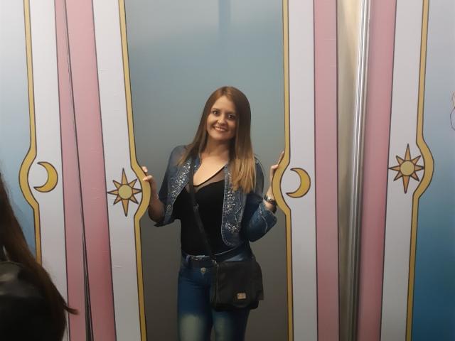LaurenSpitz stands confidently between ornate pink and white doors with gold accents. She wears a black V-neck top, sparkly jacket, and jeans, smiling directly at the camera. Fucking hot.