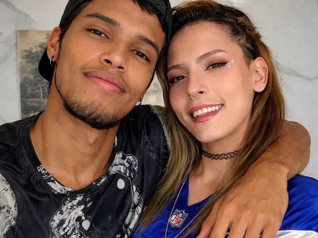 Close-up van KatyAndDante en KatyAndDante, een aantrekkelijk stel. KatyAndDante heeft een bruine huid, zwart haar en een zelfverzekerde grijns. KatyAndDante heeft een bleke huid, bruin haar, een neusring en een verleidelijke glimlach. KatyAndDante's arm om de schouder van KatyAndDante..