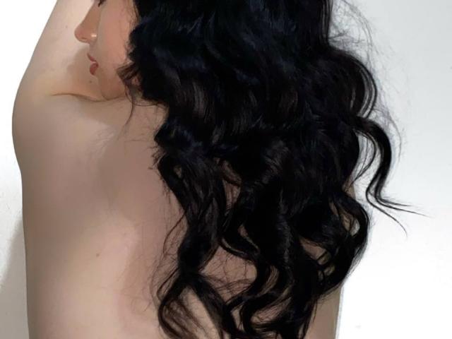 Foto van een naakt persoon met lang, golvend zwart haar dat hun bovenrug en schouder bedekt. Bleke huid, zichtbare schouderblad, zacht licht dat de haartextuur accentueert. Heel aantrekkelijk, het contrast met het donkere haar..