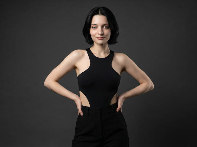 Photorealistic CGI of MelyndaMarron with short black hair, pale skin, and a confident stance, wearing a black sleeveless dress with side cutouts, hands on hips, dark background. Fucking sexy.